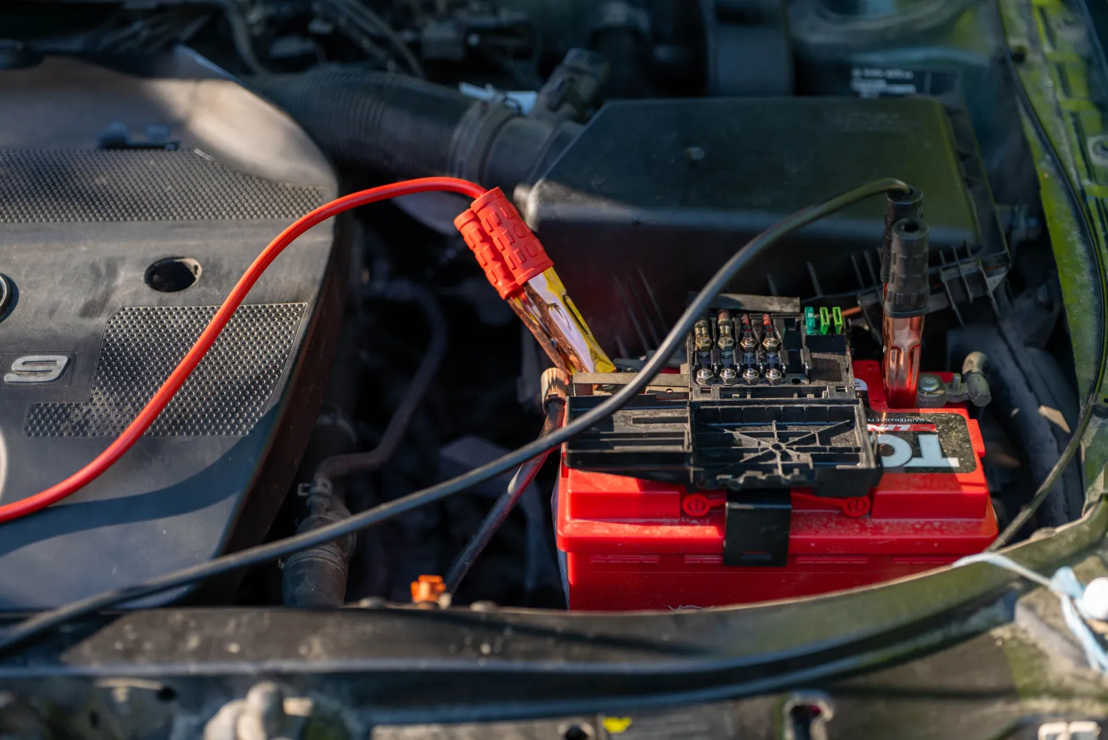 Røde startkabler koblet til bilbatteriet i et motorrom